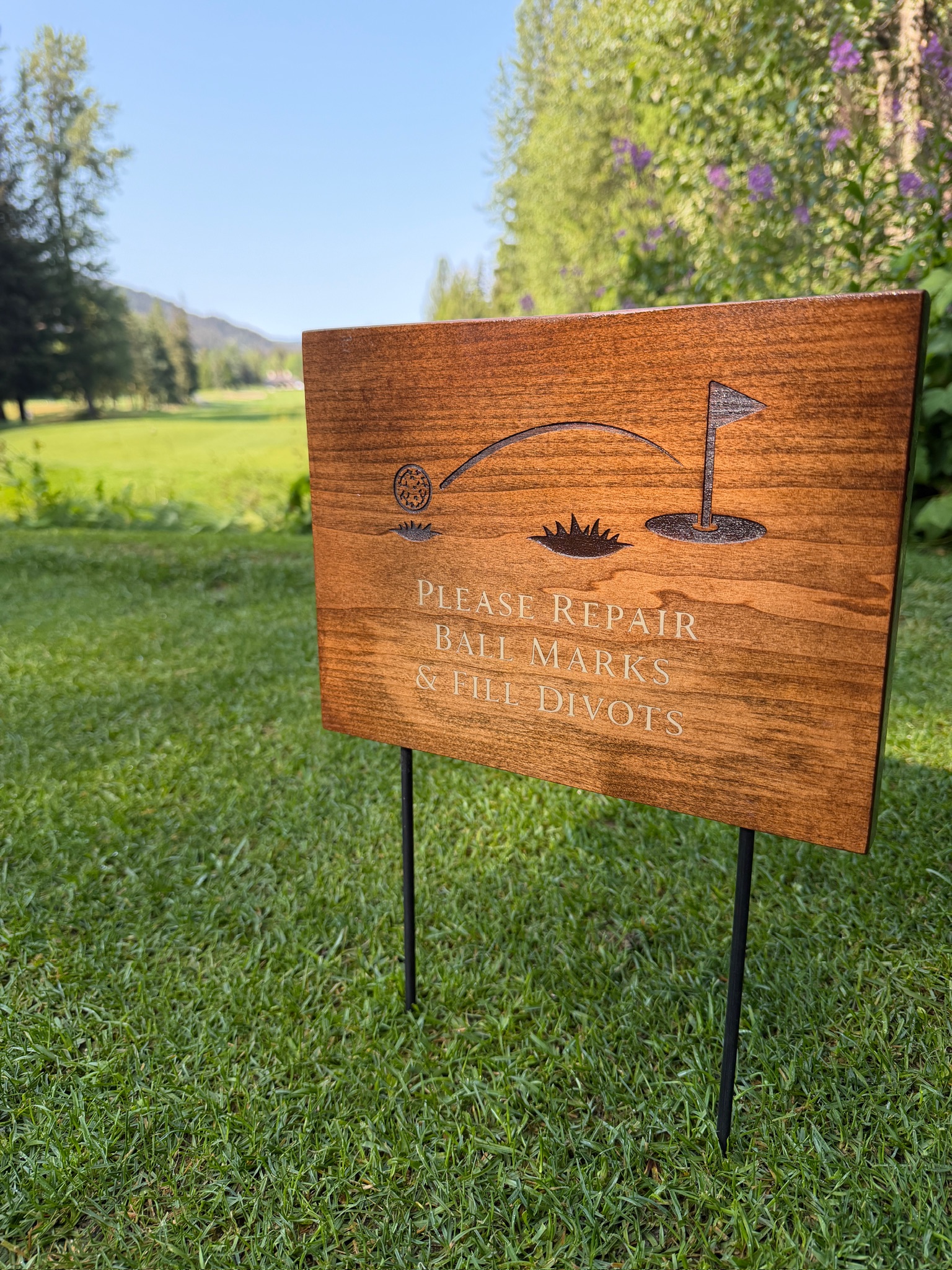 Walnut course sign reading Please Repair Ball Marks and Fill Divots with engraved flag and green graphic, mounted on steel stakes on a golf course.