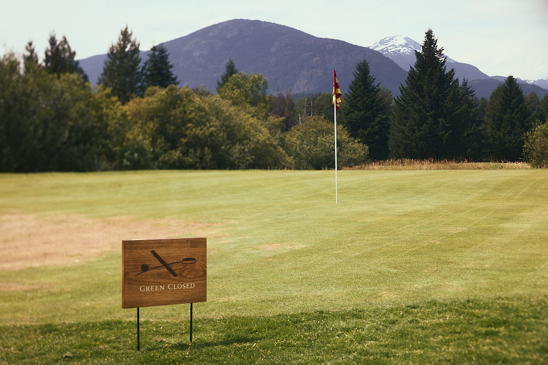 Wooden Green Closed course sign with engraved graphic on steel stakes, with flagstick and mountain backdrop.