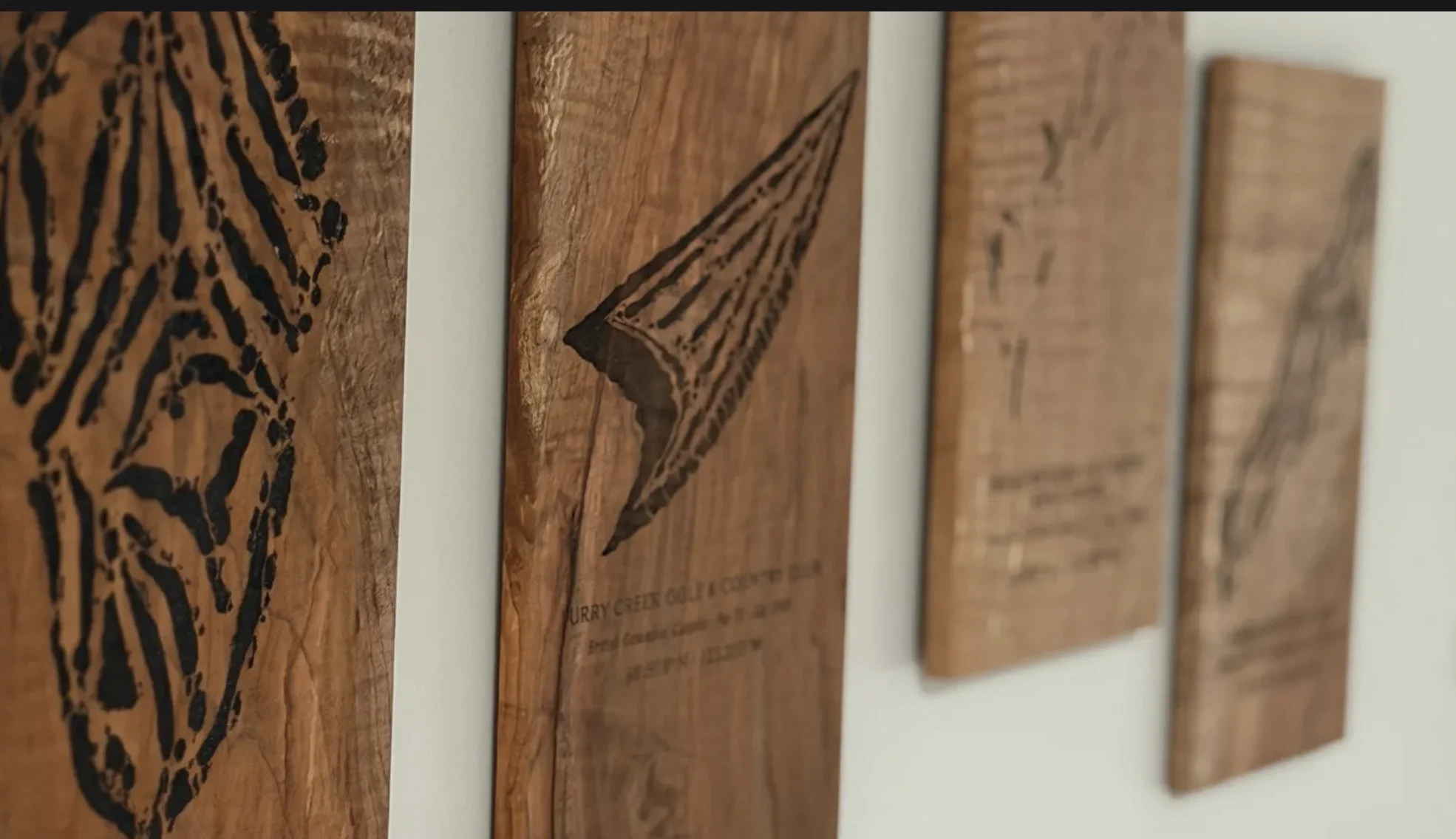 Row of handcrafted wooden plaques with engraved topographic course maps, leaning against a white wall.