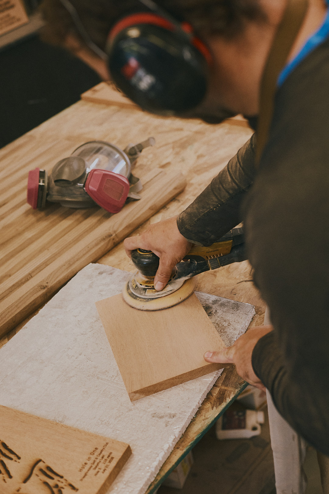 Ben sanding a plaque on the studio workbench, orbital sander in hand.