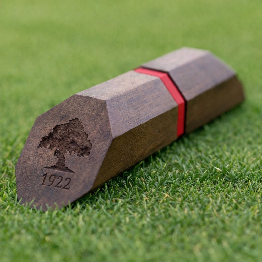 Faceted walnut tee marker with engraved tree crest on turf.