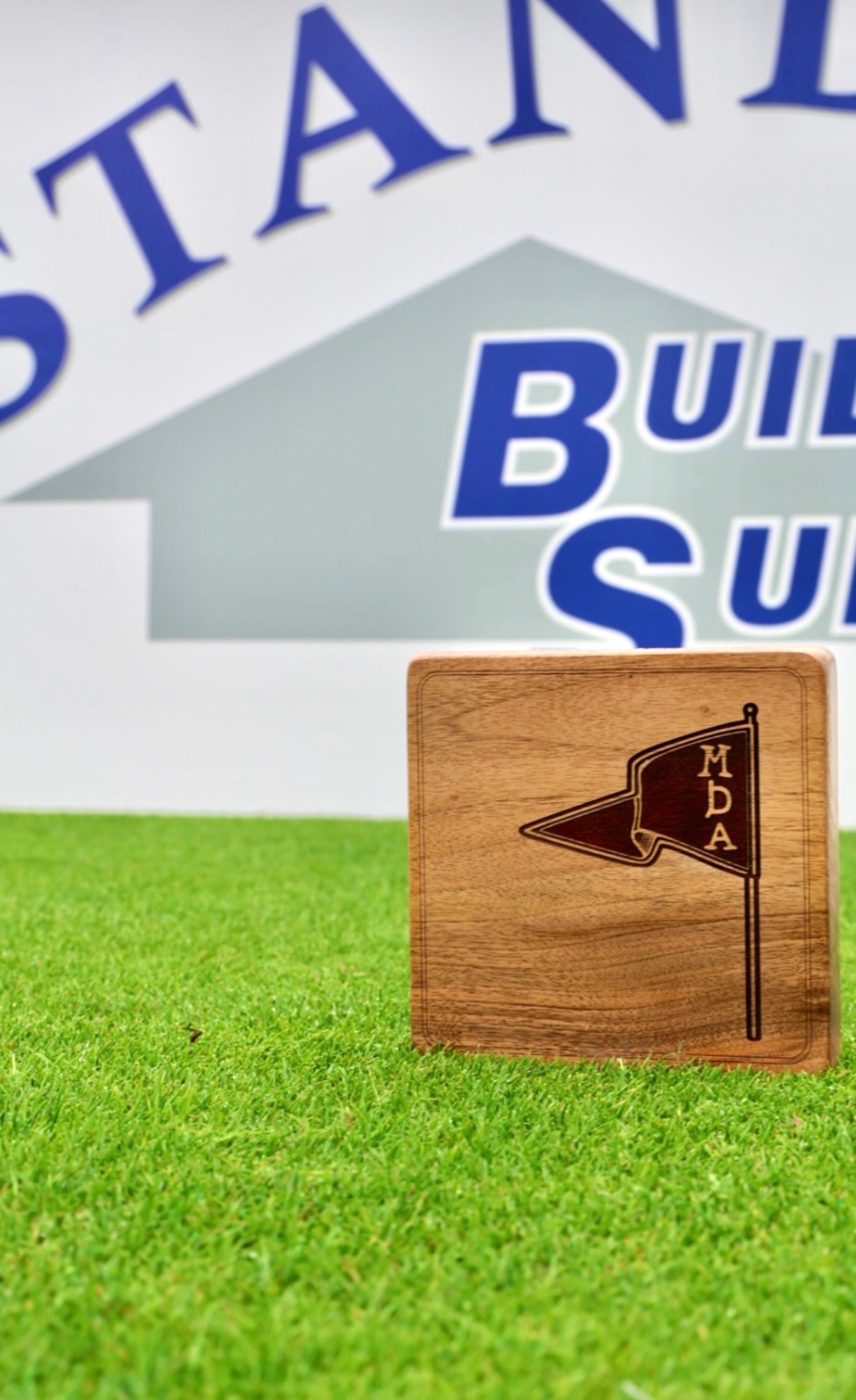 English walnut tournament tee marker with engraved pennant flag and MDA lettering, set on turf.